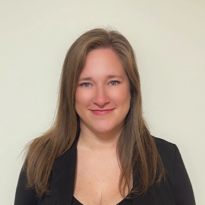 Office Manager Abby In Black Top Smiling In Front Of Beige Wall