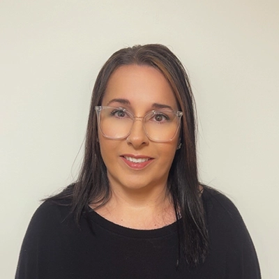 Patient Care Coordinator April In Black Top Smiling In Front Of Beige Wall