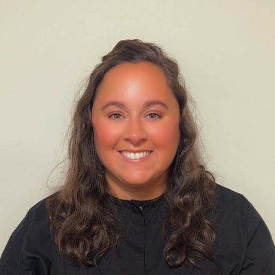 Dental Hygienist Cindy In Black Top Smiling In Front Of Beige Wall