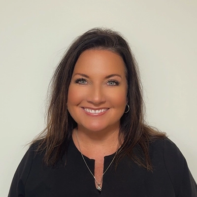Dental Hygienist Marcia In Black Top Smiling In Front Of Beige Wall