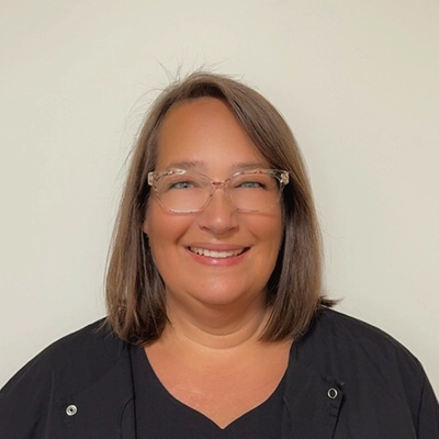 Dental Assistant Terri In Black Top Smiling In Front Of Beige Wall