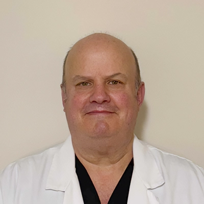 Dentist Timothy Towle In Lab Coat Smiling In Front Of Beige Wall