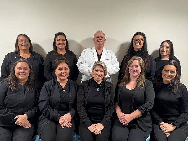Dentist Timothy Towle With Team Smiling In Front Of A Beige Wall